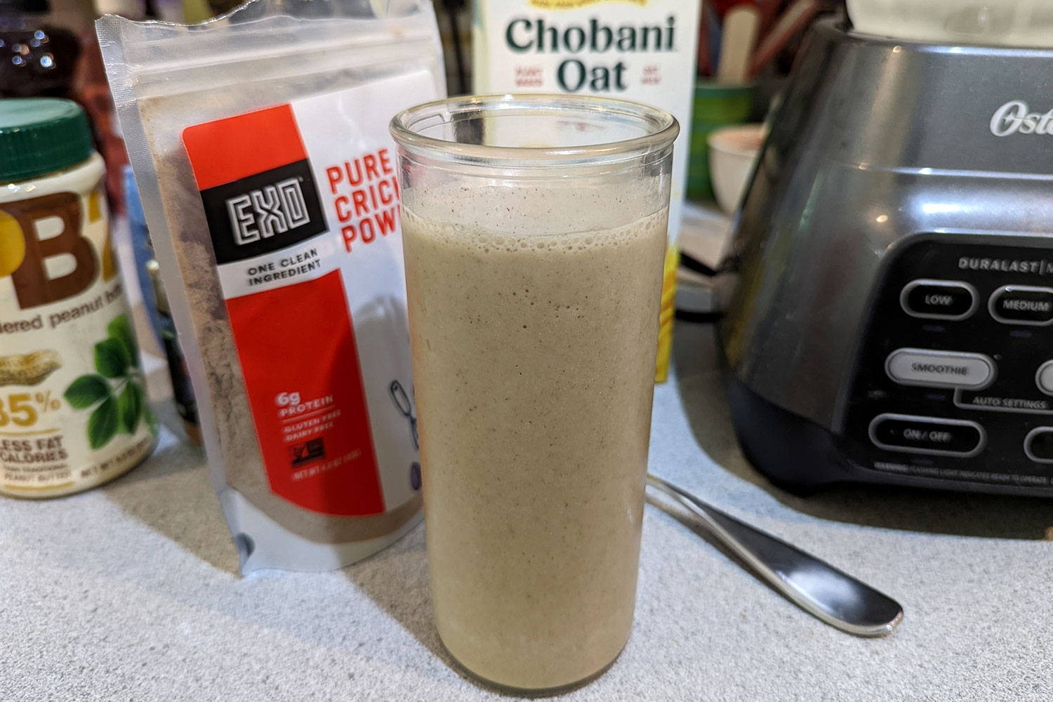 Light brown smoothie in glass cup placed in front of a bag of pure cricket powder