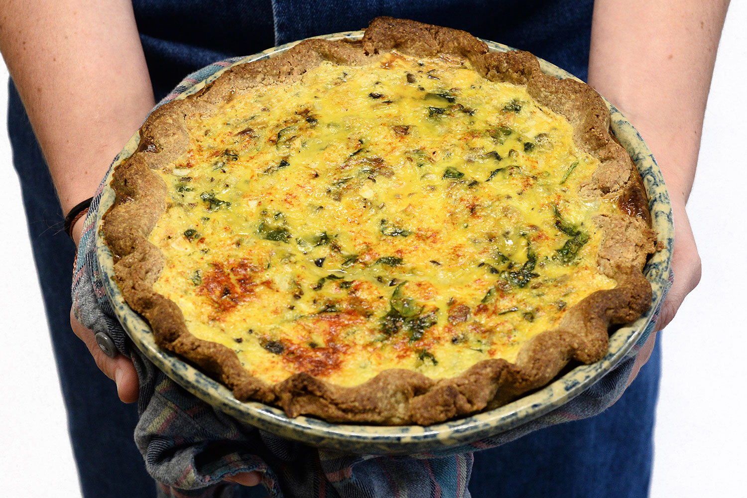 Person holding quiche in dish with kitchen cloth