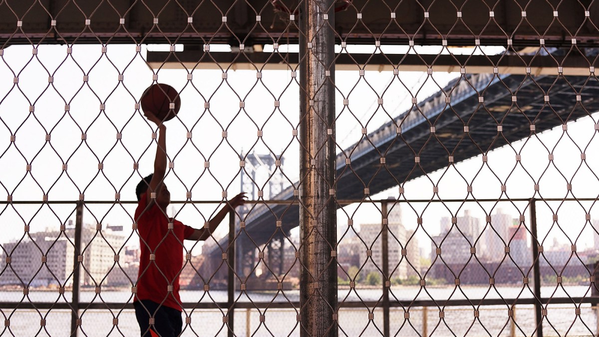 A teen plays basketball in the shade of a bridge along Manhattan's East River on August 27, 2014 in New York City.