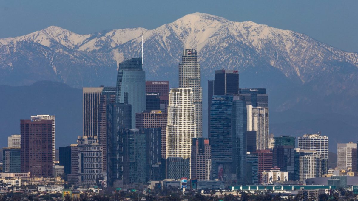A photo of downtown Los Angeles buildings against backdrop of clear snow-capped mountains and blue skies