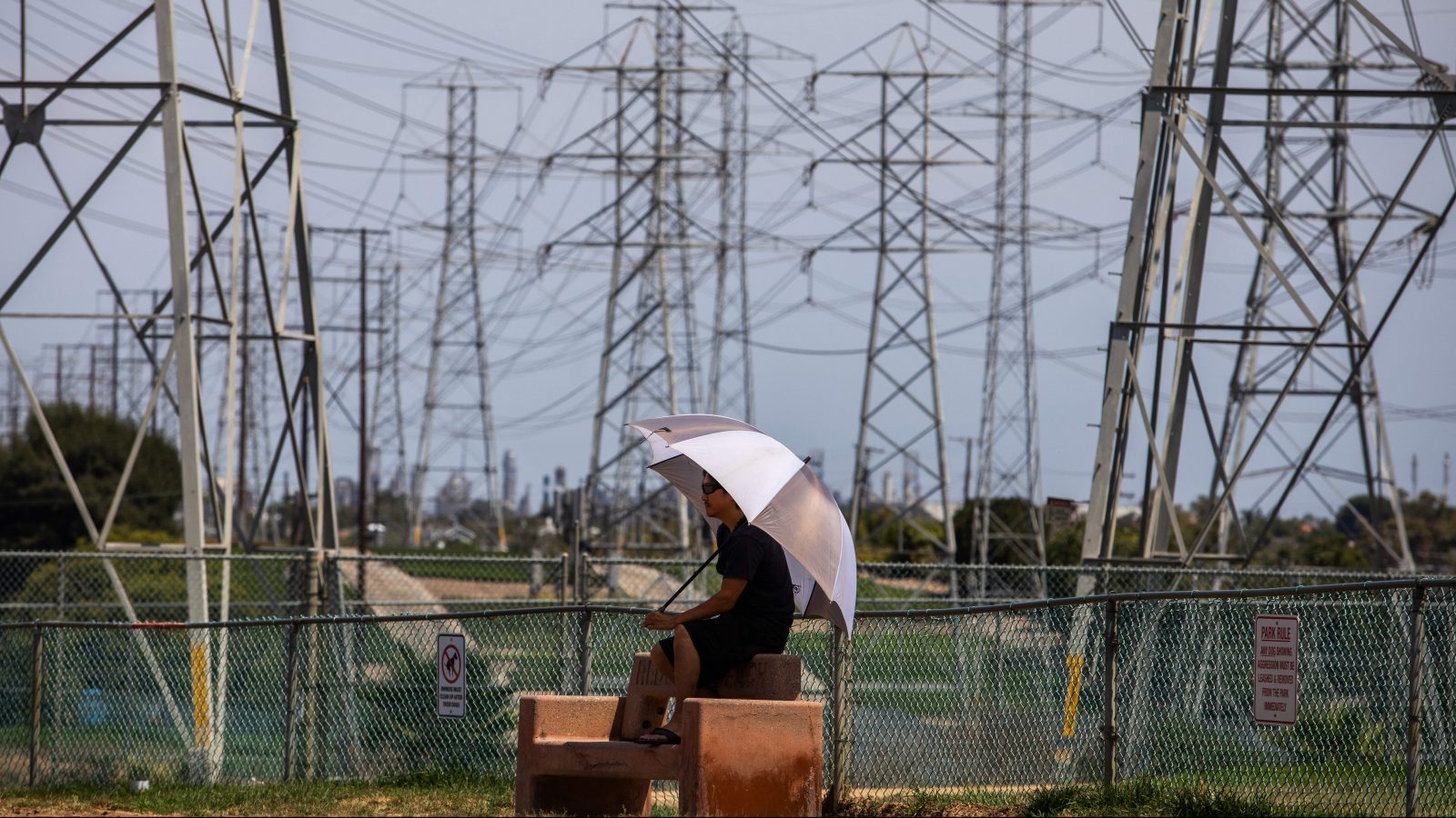 A man sits in the shade of his umbrella at the Dog Park under high tension power lines in Redondo Beach, California on August 16, 2020.