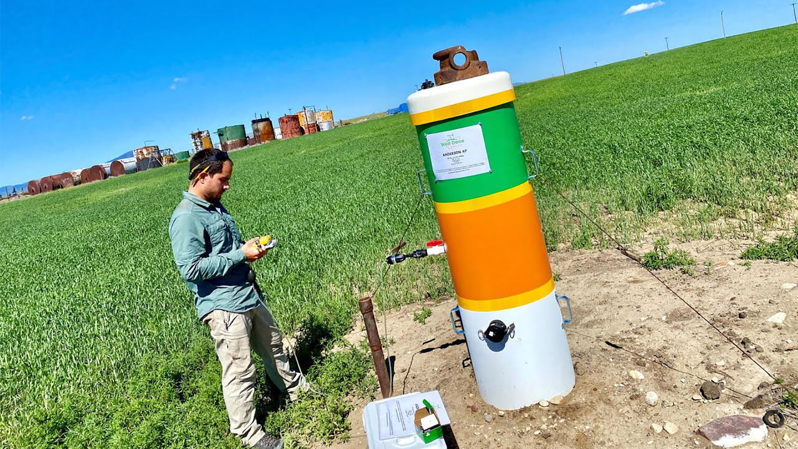 Photo of man standing in front of abandoned oil well taking samples