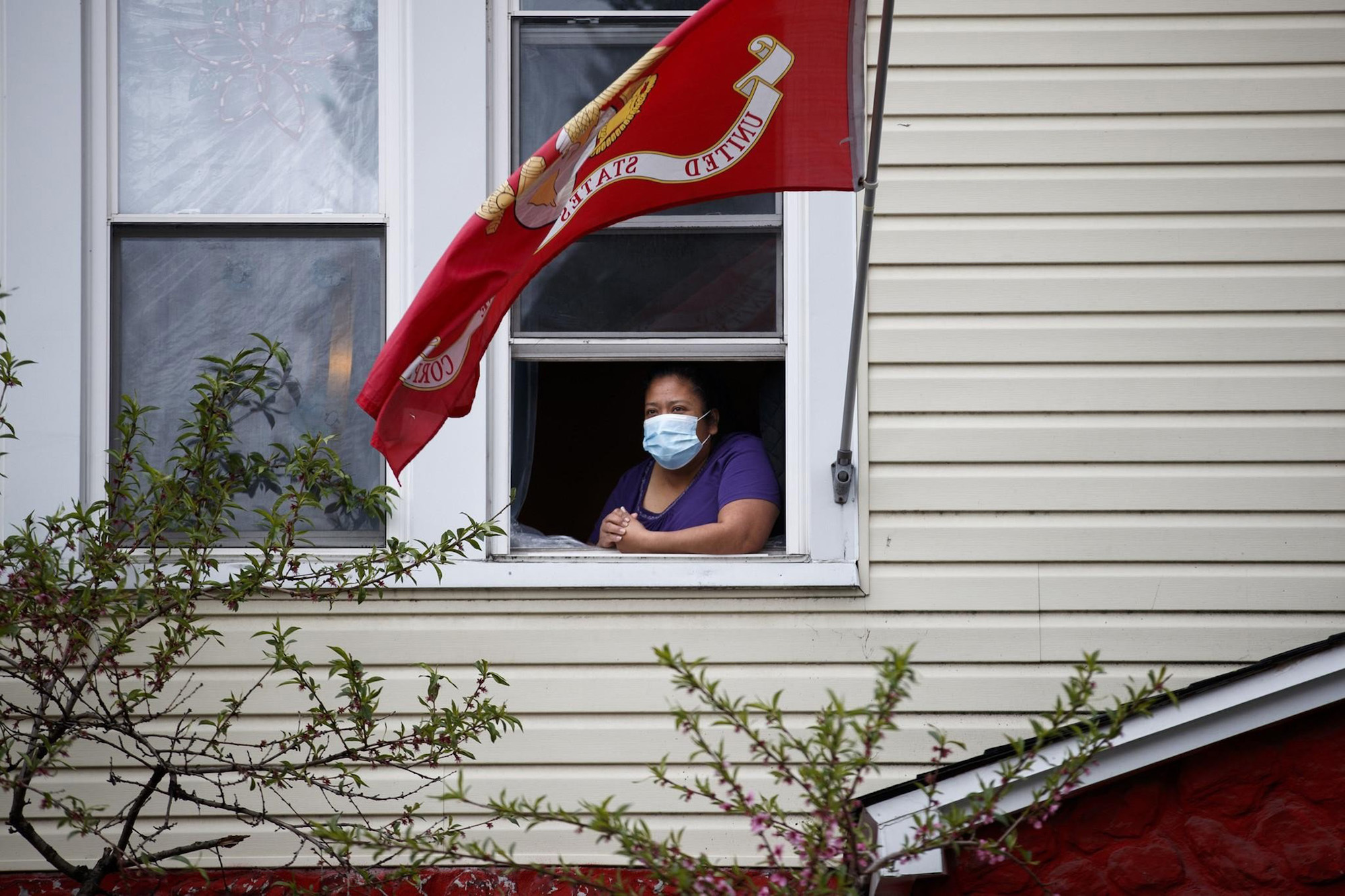 a photo of a woman wearing a surgical mask looking out the window of her home
