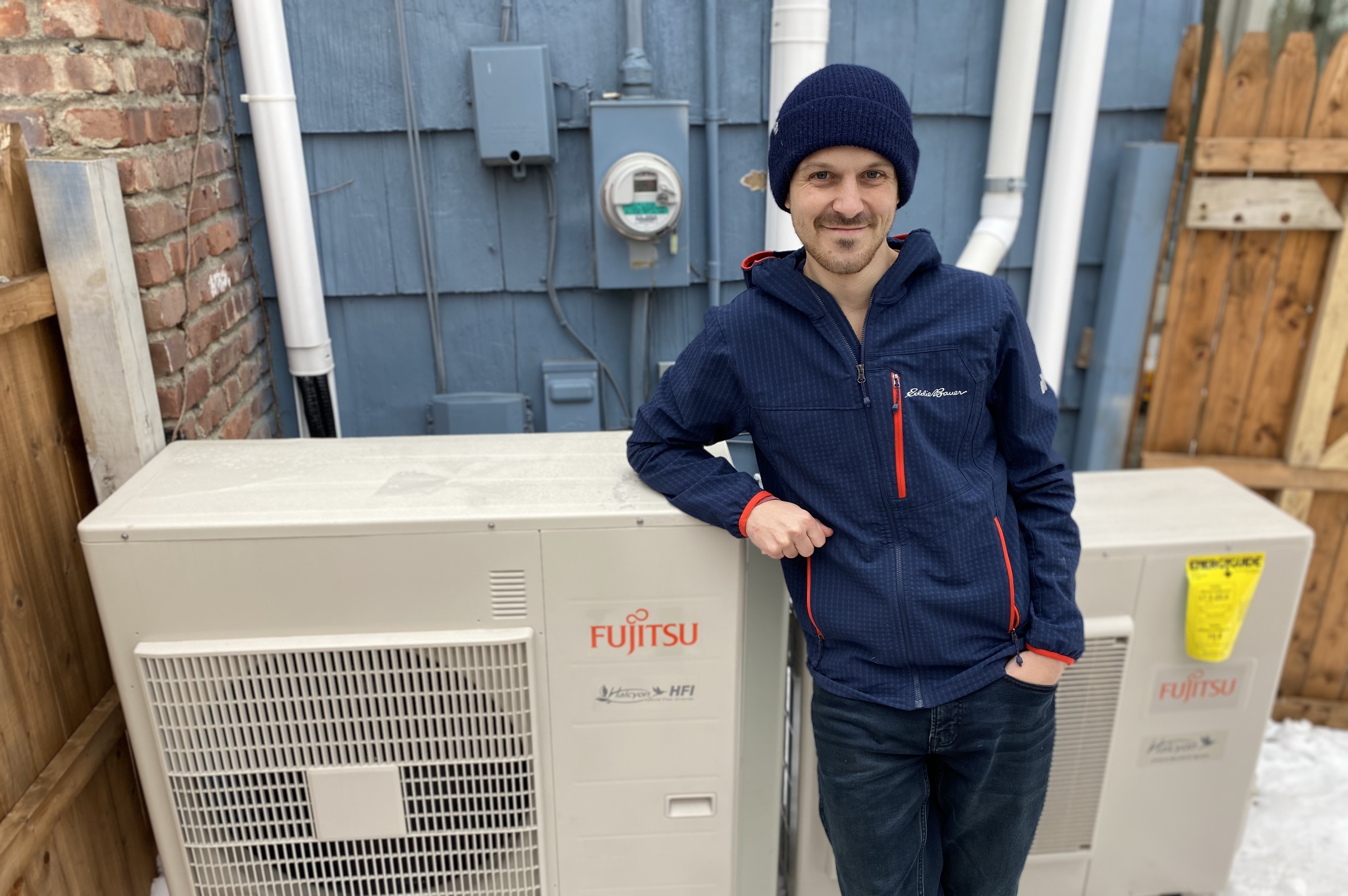 Adam James standing next to the outdoor unit of his new heat pump