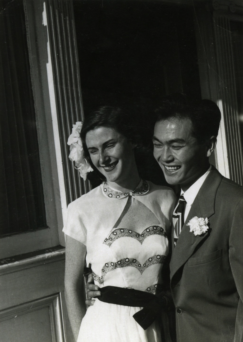 A black and white photo of Dorothy Walker and Joe Kamiya with their arms around each other and smiling in front of a house