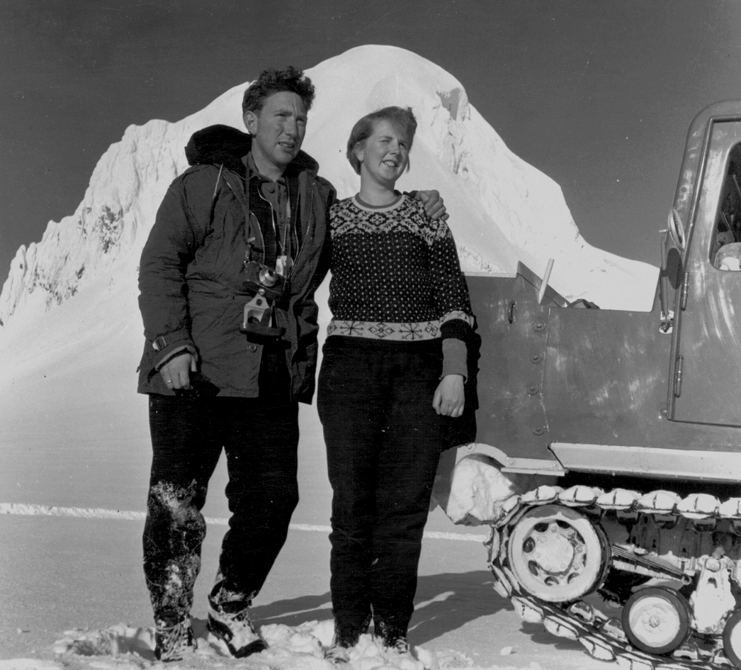 A black-and-white photo of a bundled-up couple standing in front of a glacier.