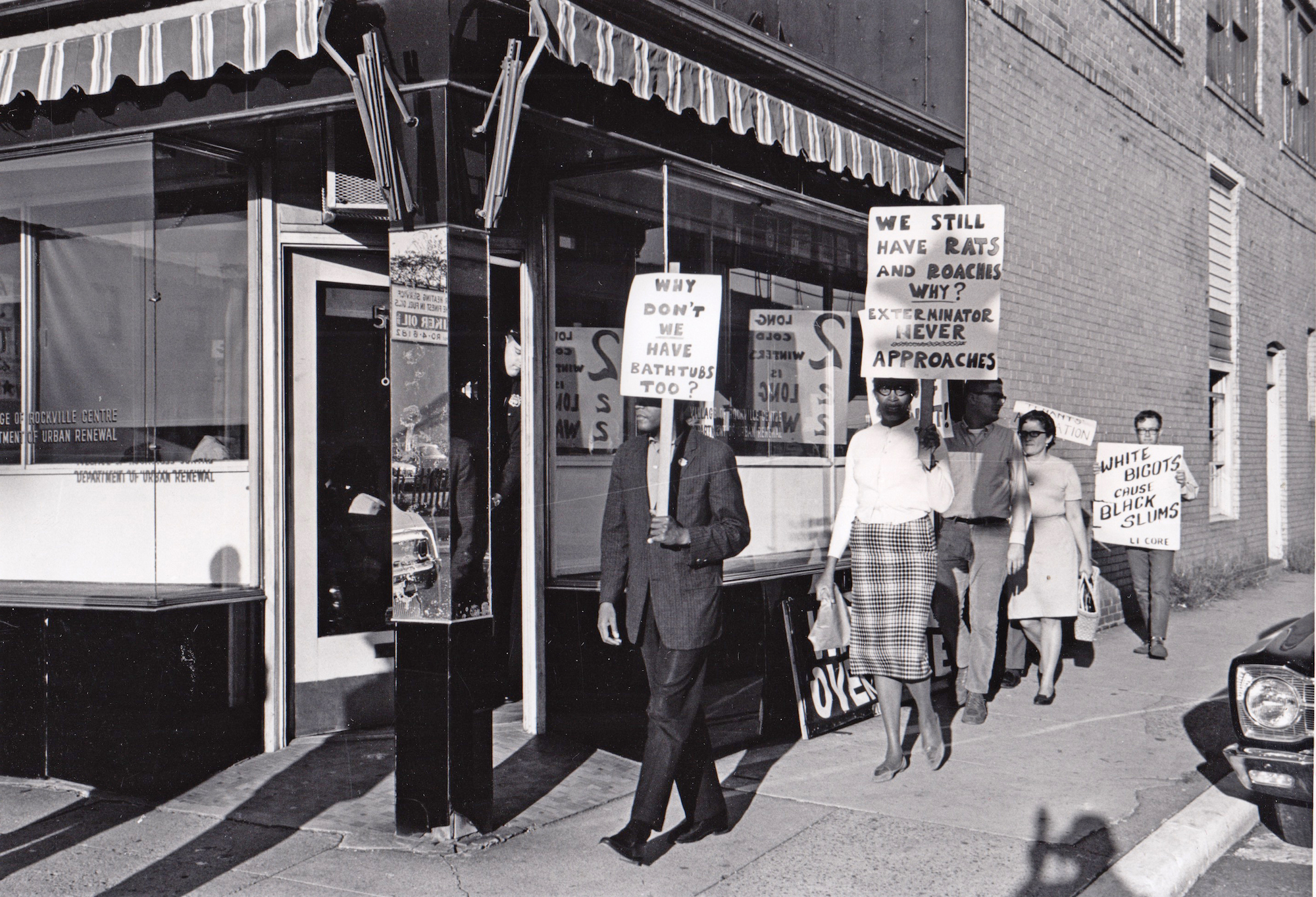 A black and white photo of a group of men and women holding picket signs outside an office