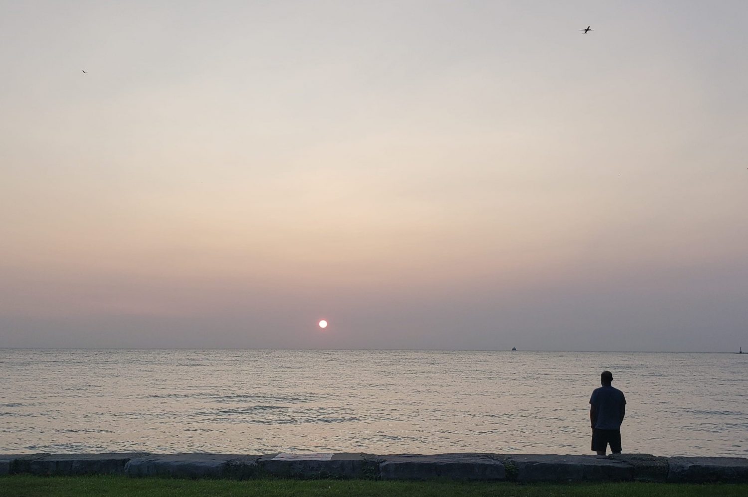 A reddish sun rises in a hazy sky over the lakefront.