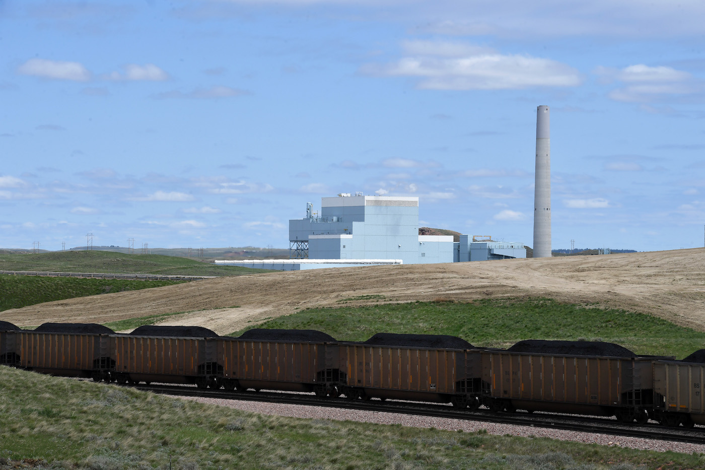 A coal plant in the distance with a train full of coal going by in the foreground