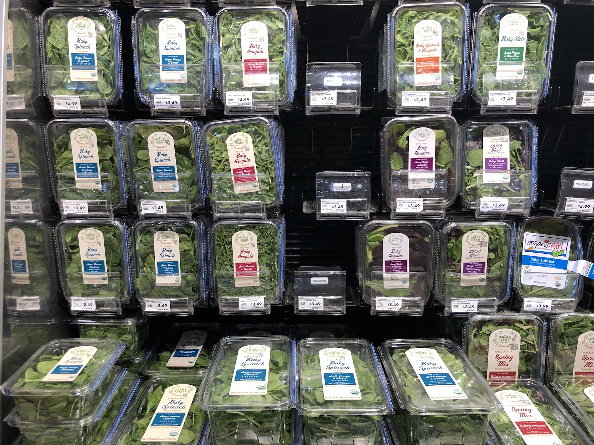 A wall of baby greens mixes each in its own plastic clamshell in a salad aisle