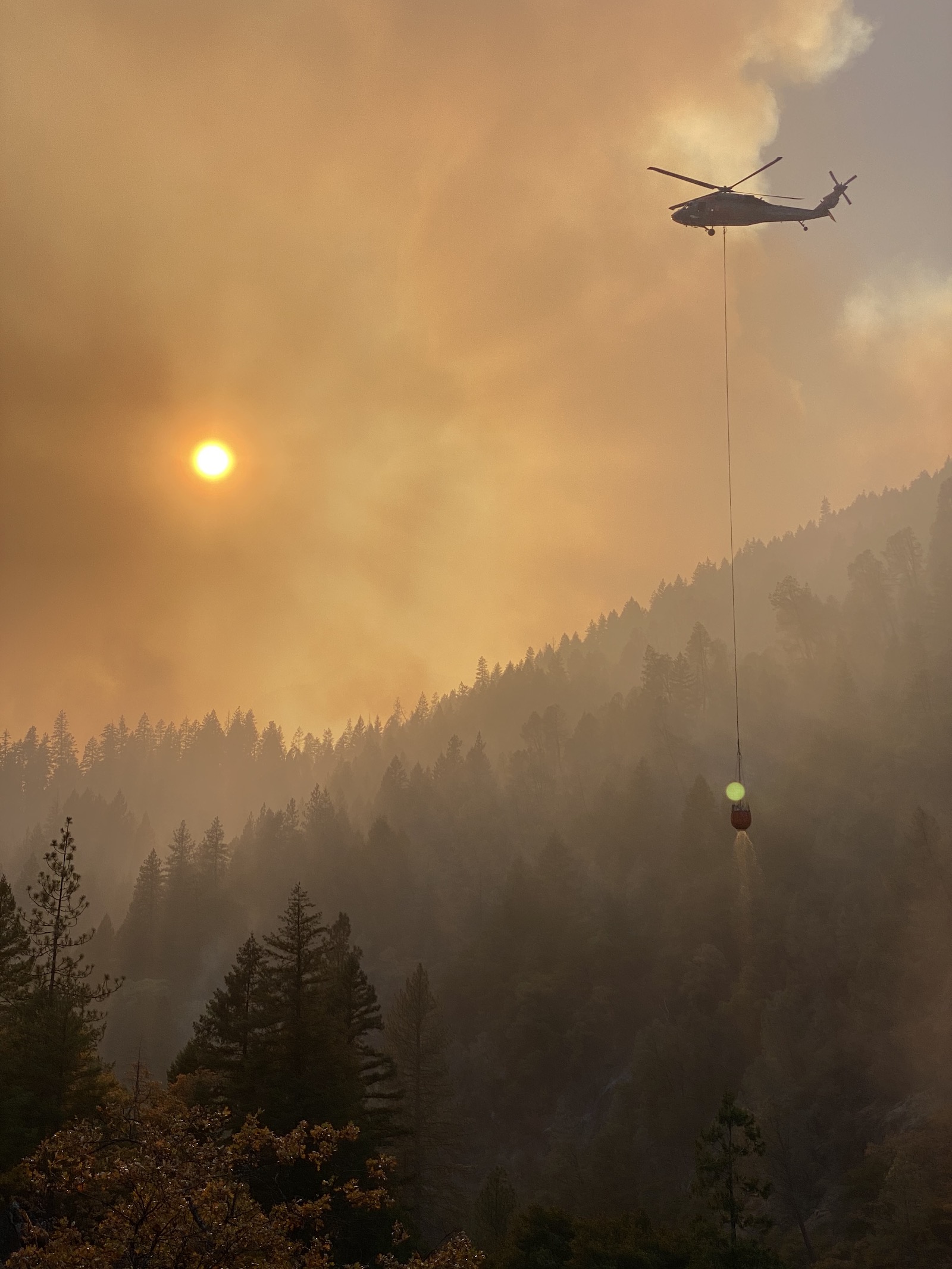a smoky daytime scene of a helicopter hovering over a forrested river area