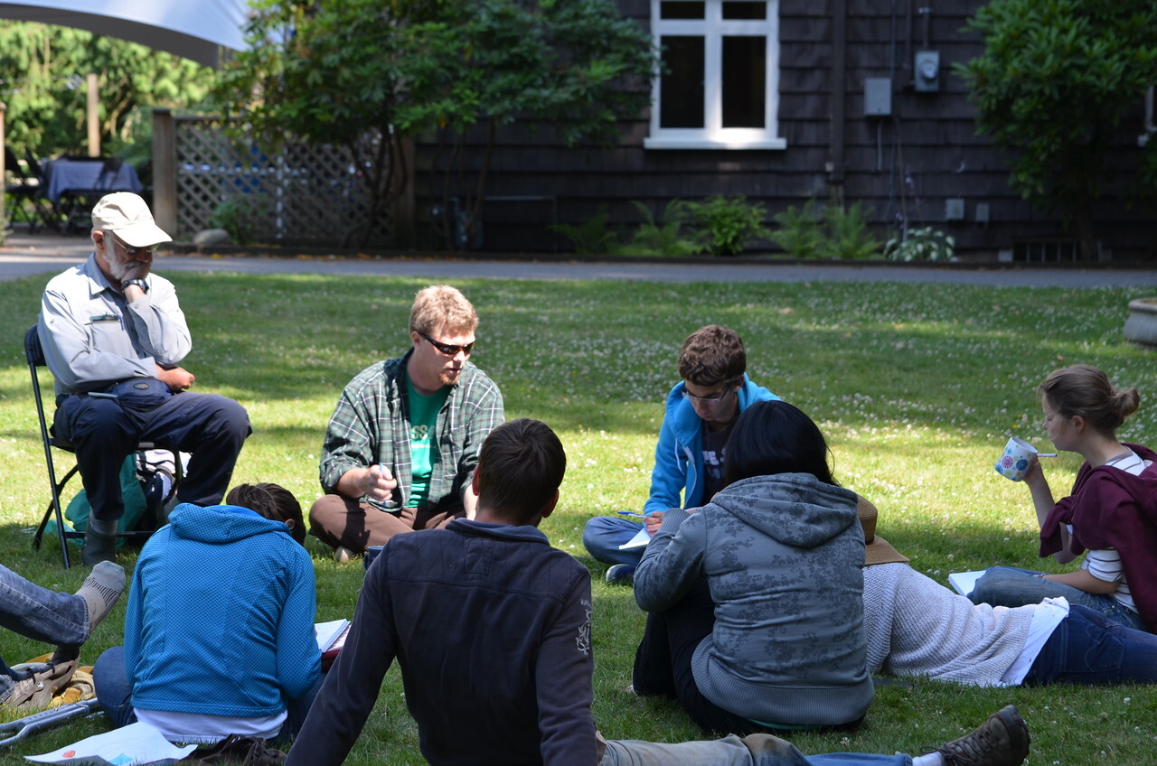 a group of people sitting in a circle in conversation on a manicured green lawn