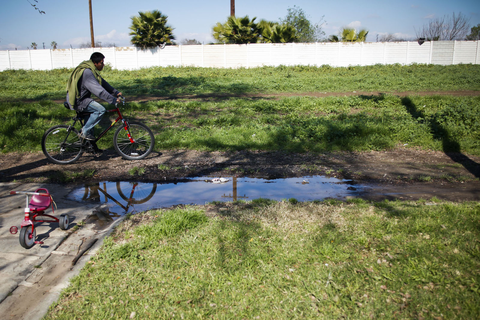 a man on a red bike pedals near a muddy pool of water in a green field
