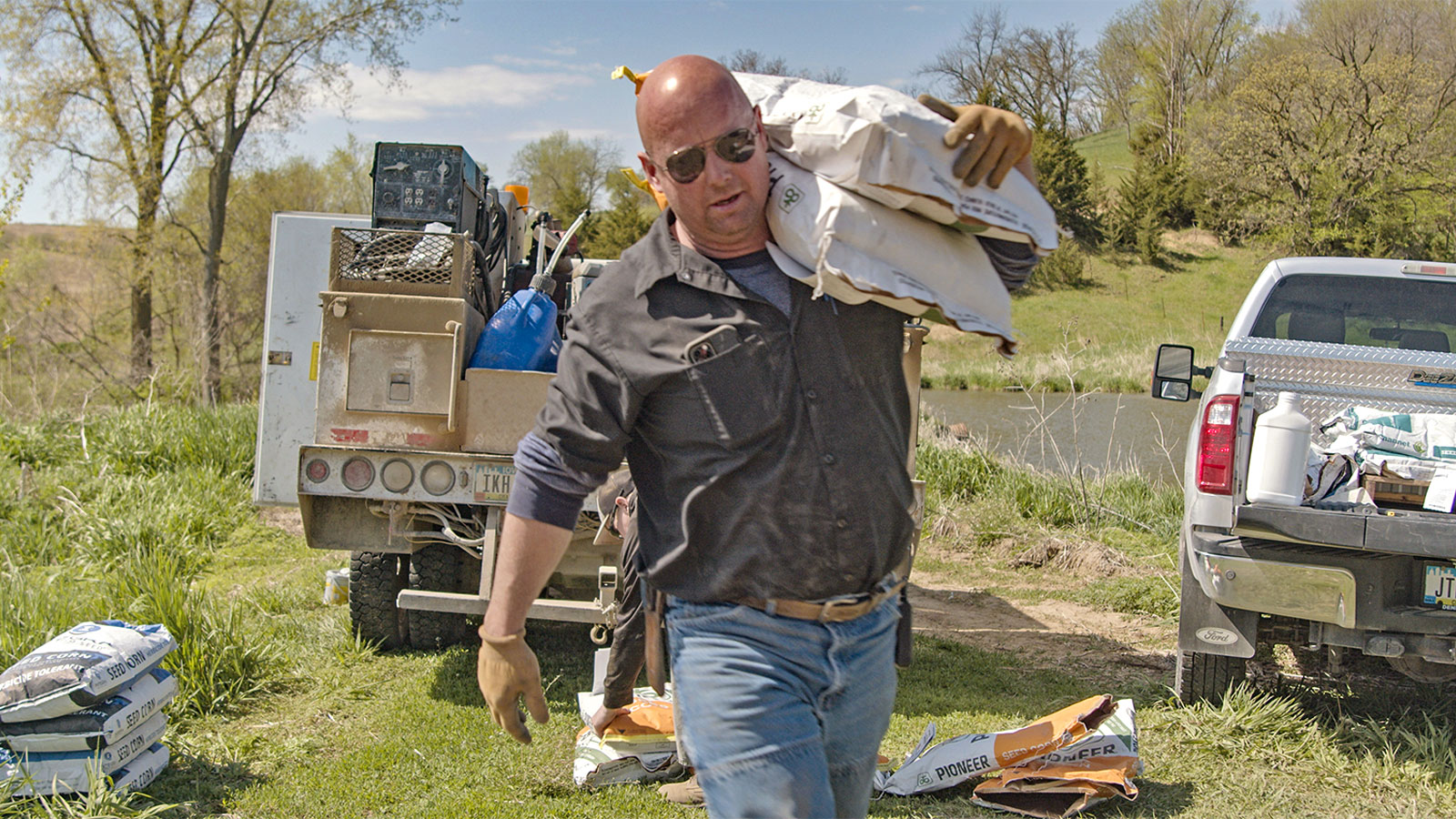 a man on a farm carries a large white sack over his shoulder