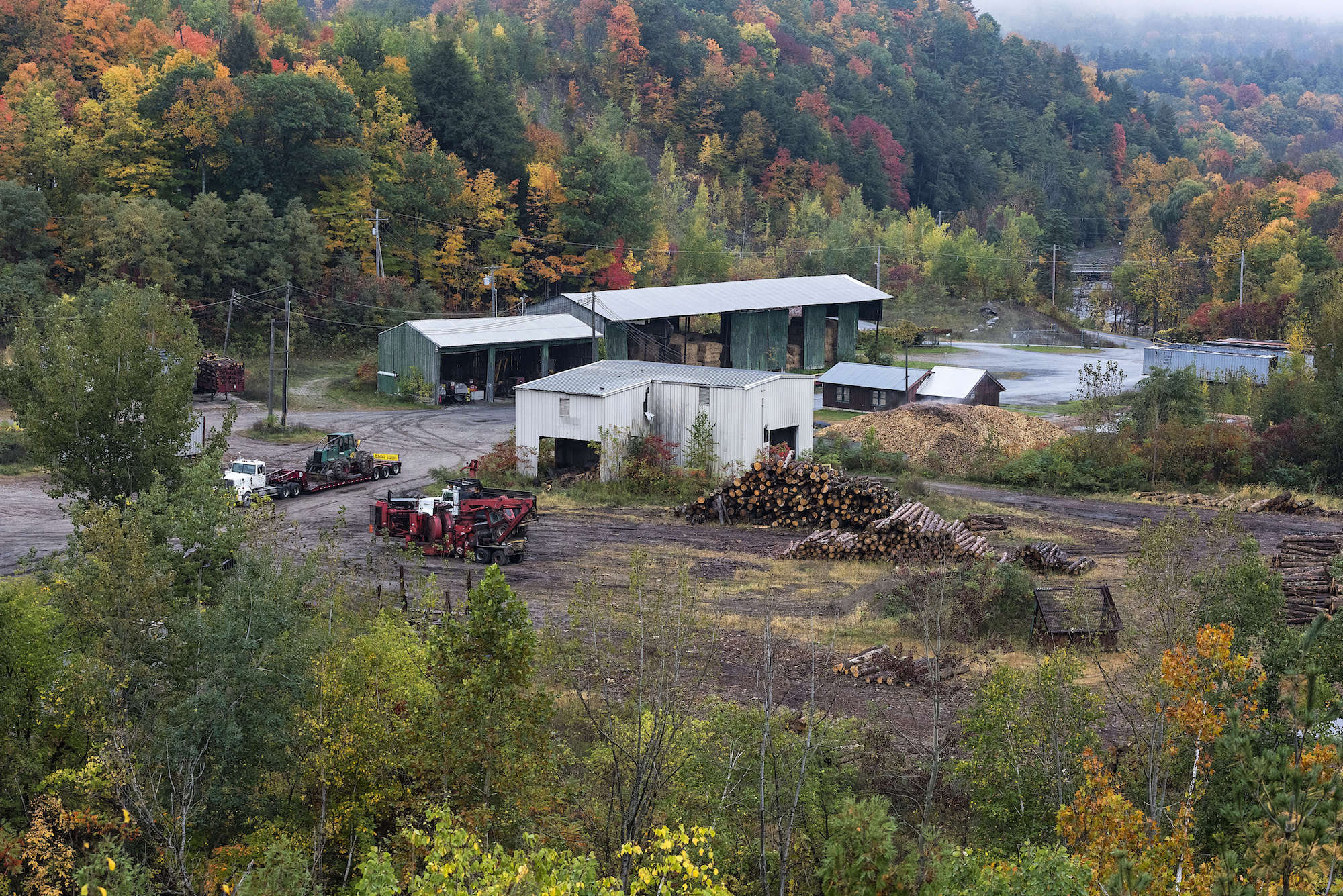 a white building with red logging equipment in the middle of fall foliage forest