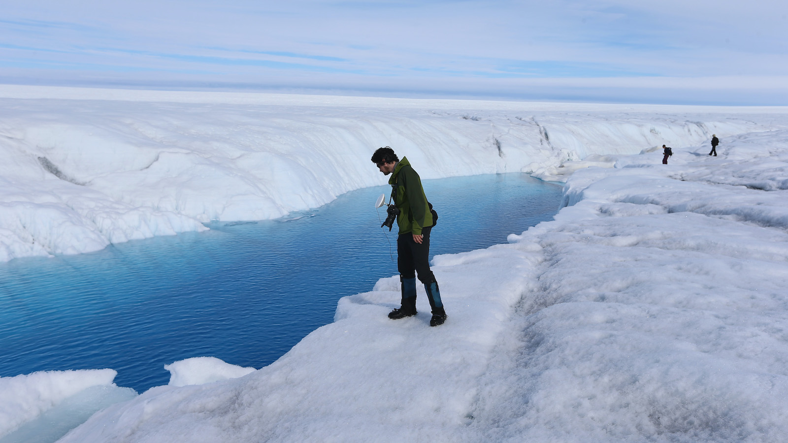 A researcher peers into the meltwater on an ice sheet.