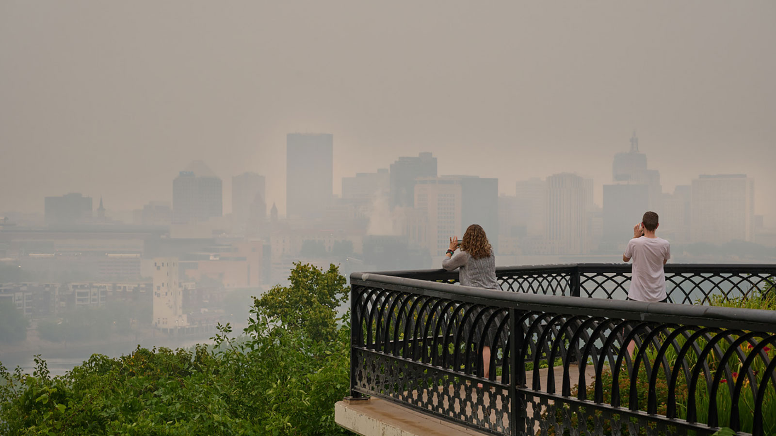 Two people in Saint Paul, Minnesota, taking photos of the city shrouded in smoke from wildfires in Canada