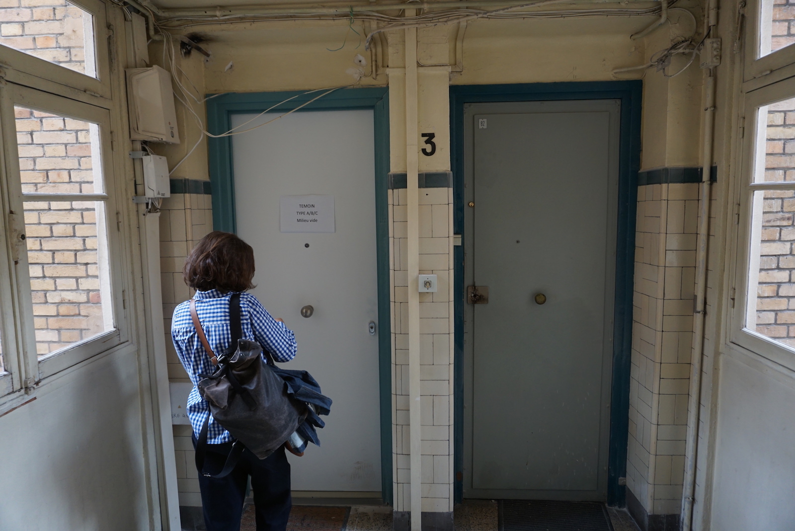 a woman faces two doors with green trim inside a small hallway