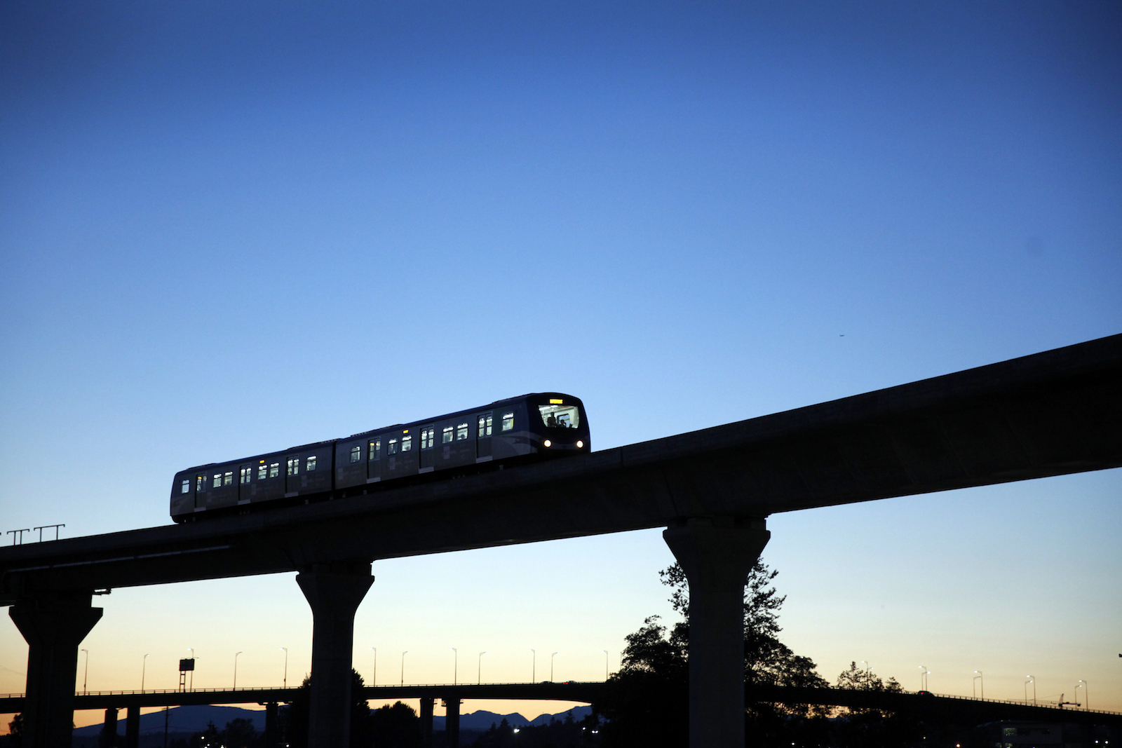 A lightrail train on an elevated road silhouetted against a darkened sky