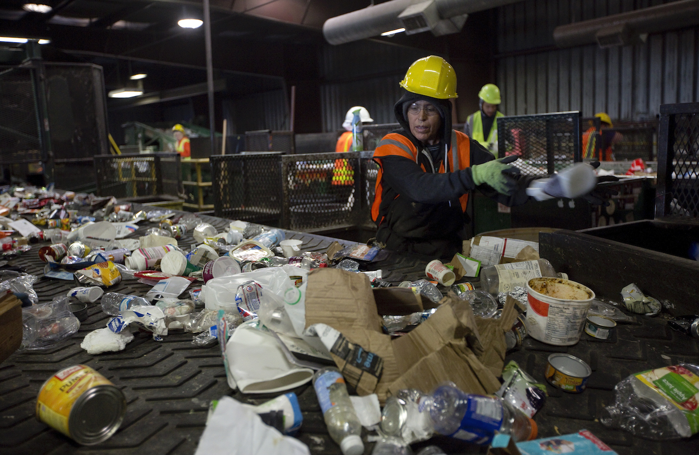 Recycling plant workers sort a stream of bottles, cardboard, and other waste.