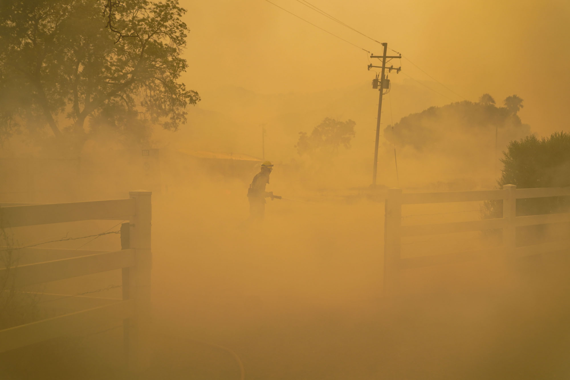 an orange smoky scene with trees, electrical wires and a lone firefighter