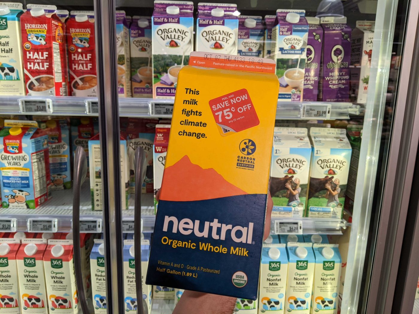 A carton of Neutral milk in front of a grocery store fridge of milk.