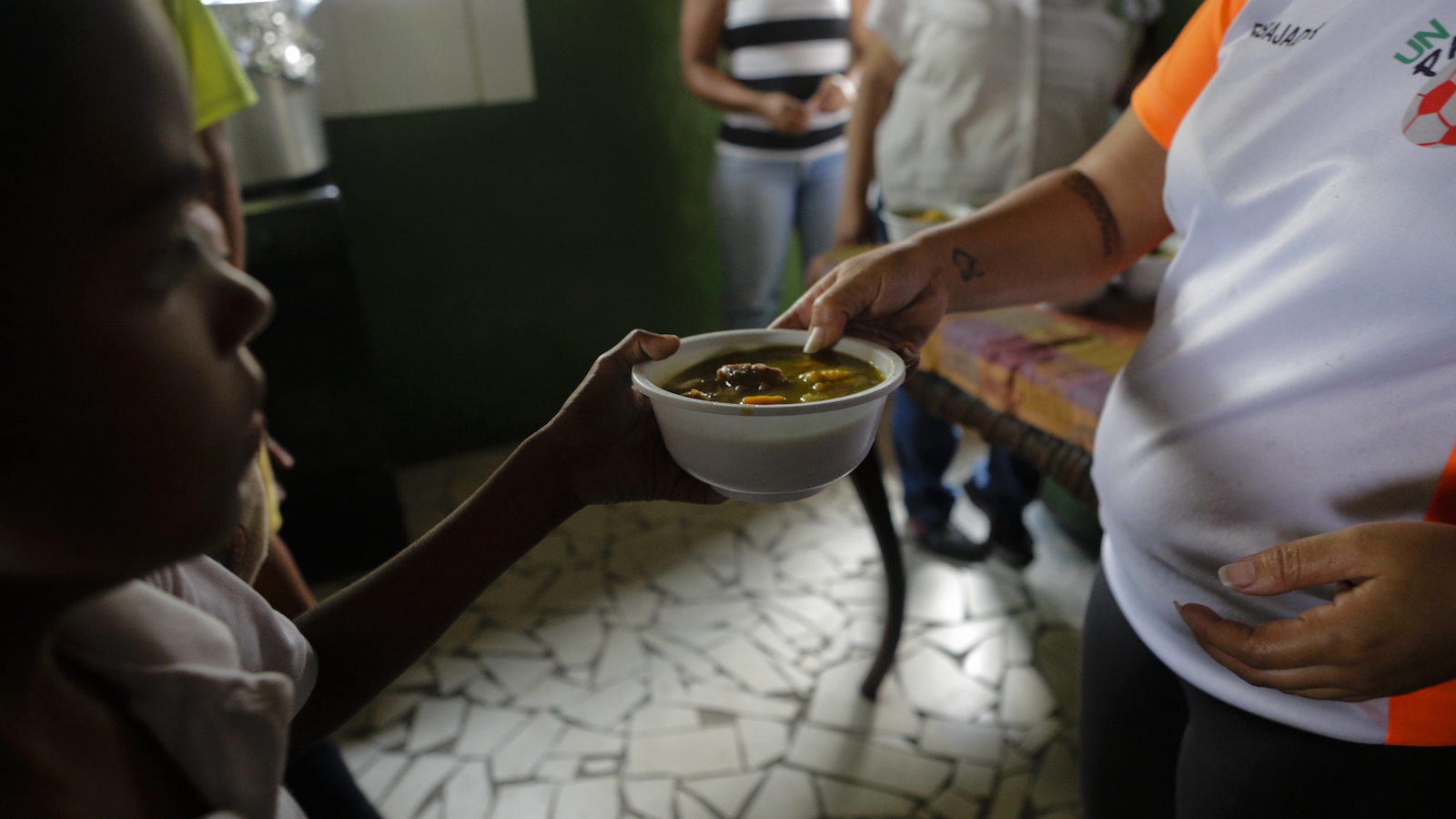 A woman hands a bowl of food to a child.