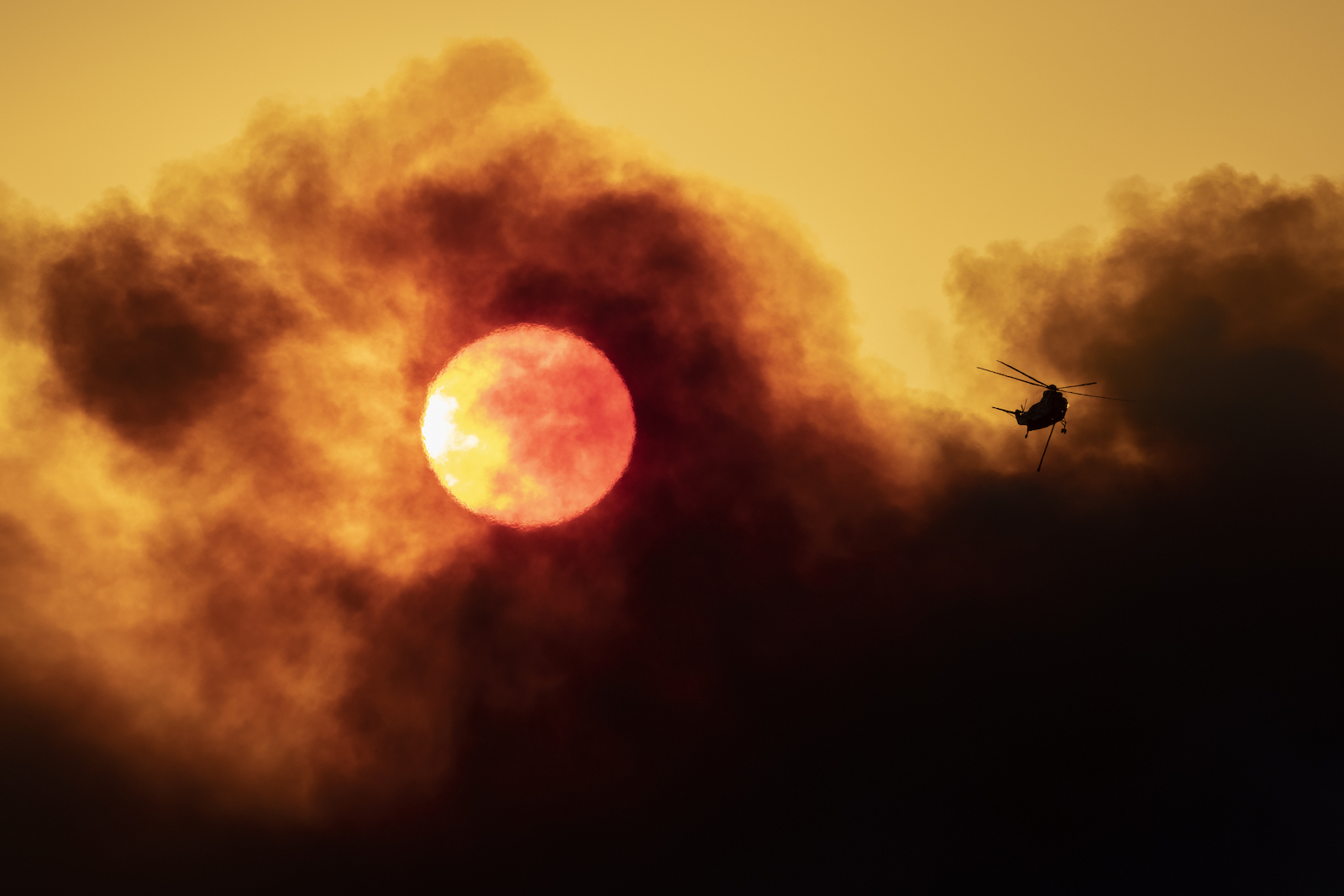 A firefighting helicopter flies as smoke from the Alisal Fire shrouds the sun on October 13, 2021 near Goleta, California. Pushed by high winds, the Alisal Fire grew to 6,000 acres overnight, shutting down the much-traveled 101 Freeway along the Pacific Coast.