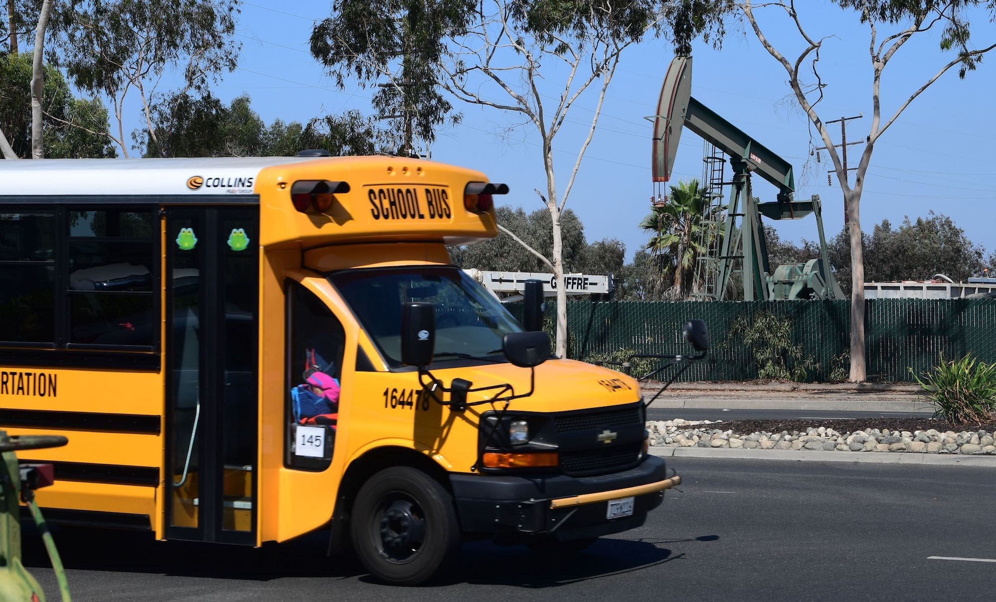 a yellow school bus parked on a street with an oil derrick visible nearby