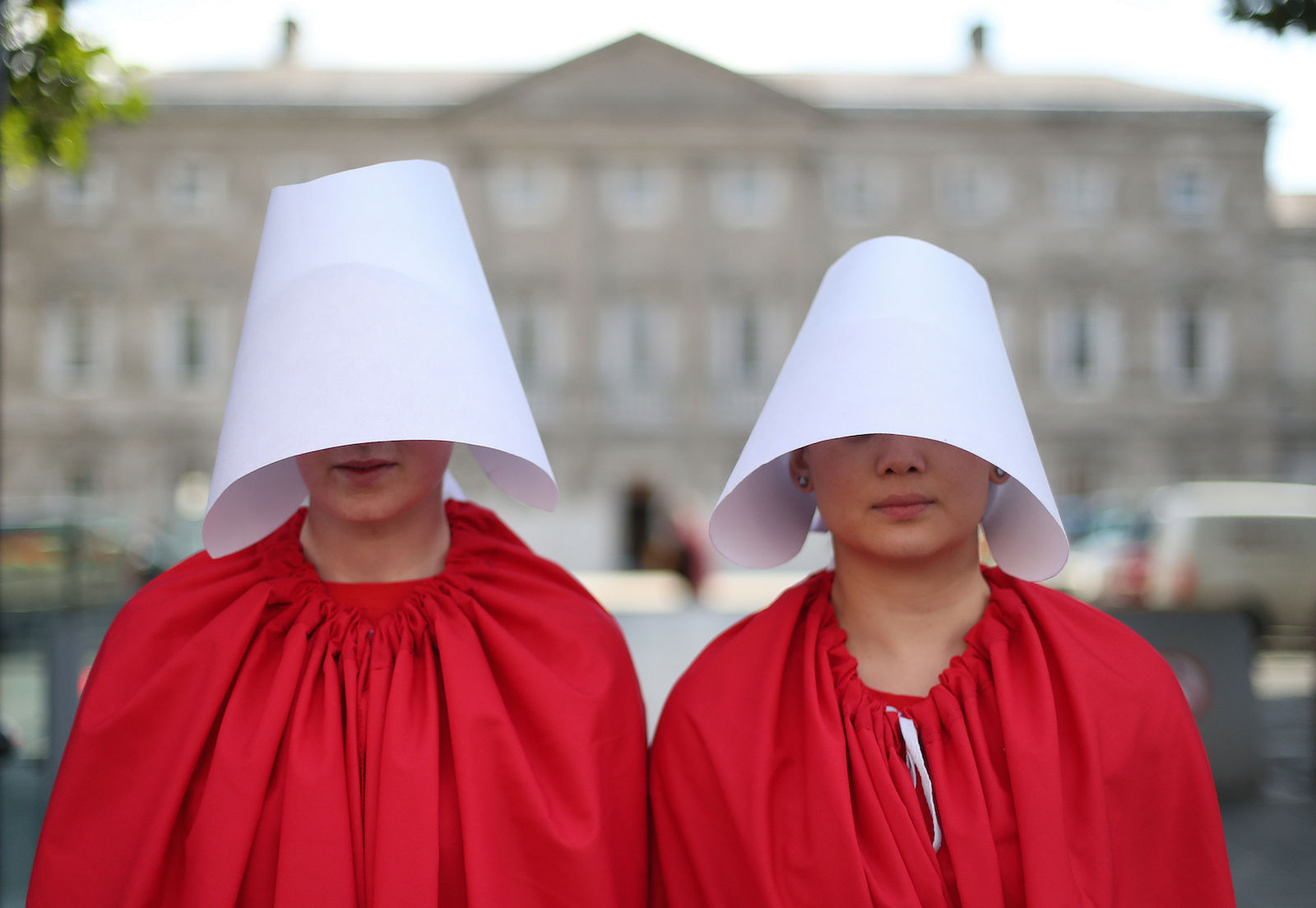 two protesters dressed in red robes and white headdresses like handmaid's tale