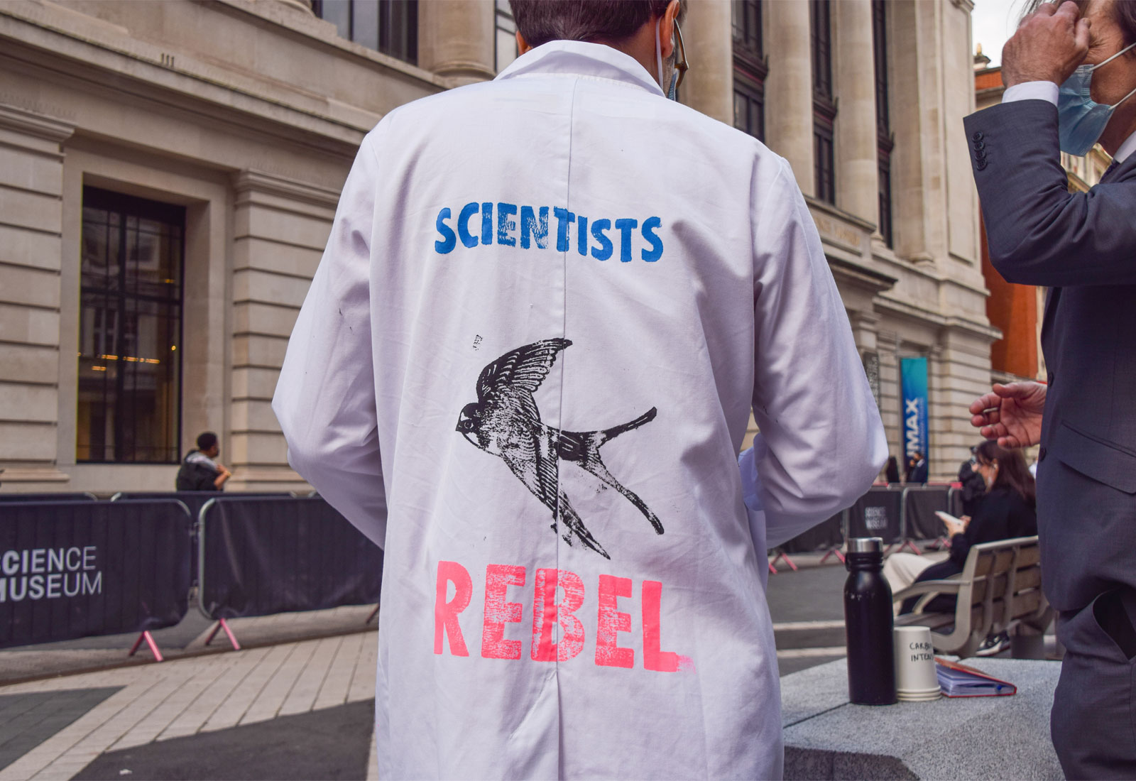 Scientist with back to camera; lab coat reads 
