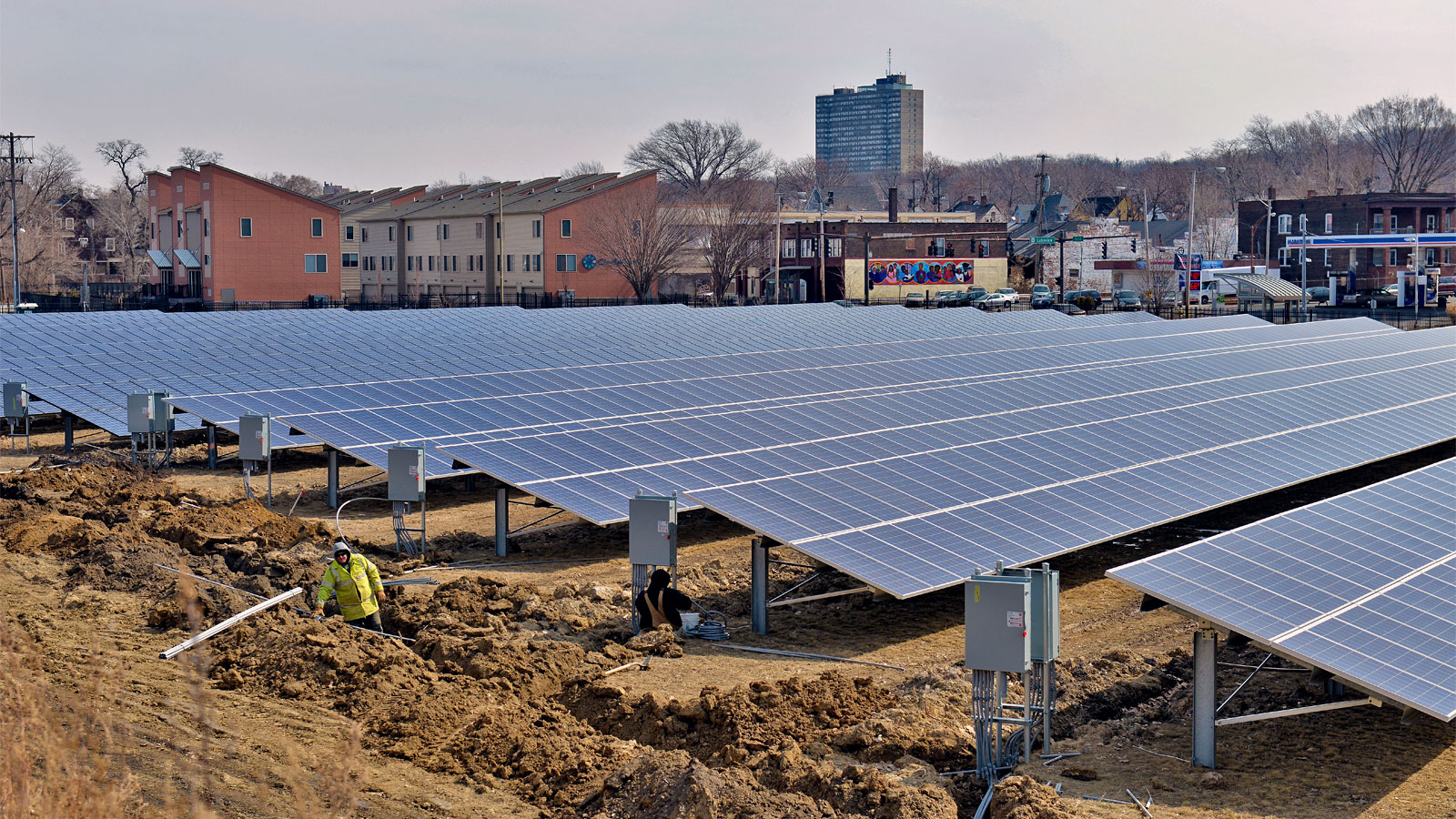 Two people installing solar panels with city buildings in the background