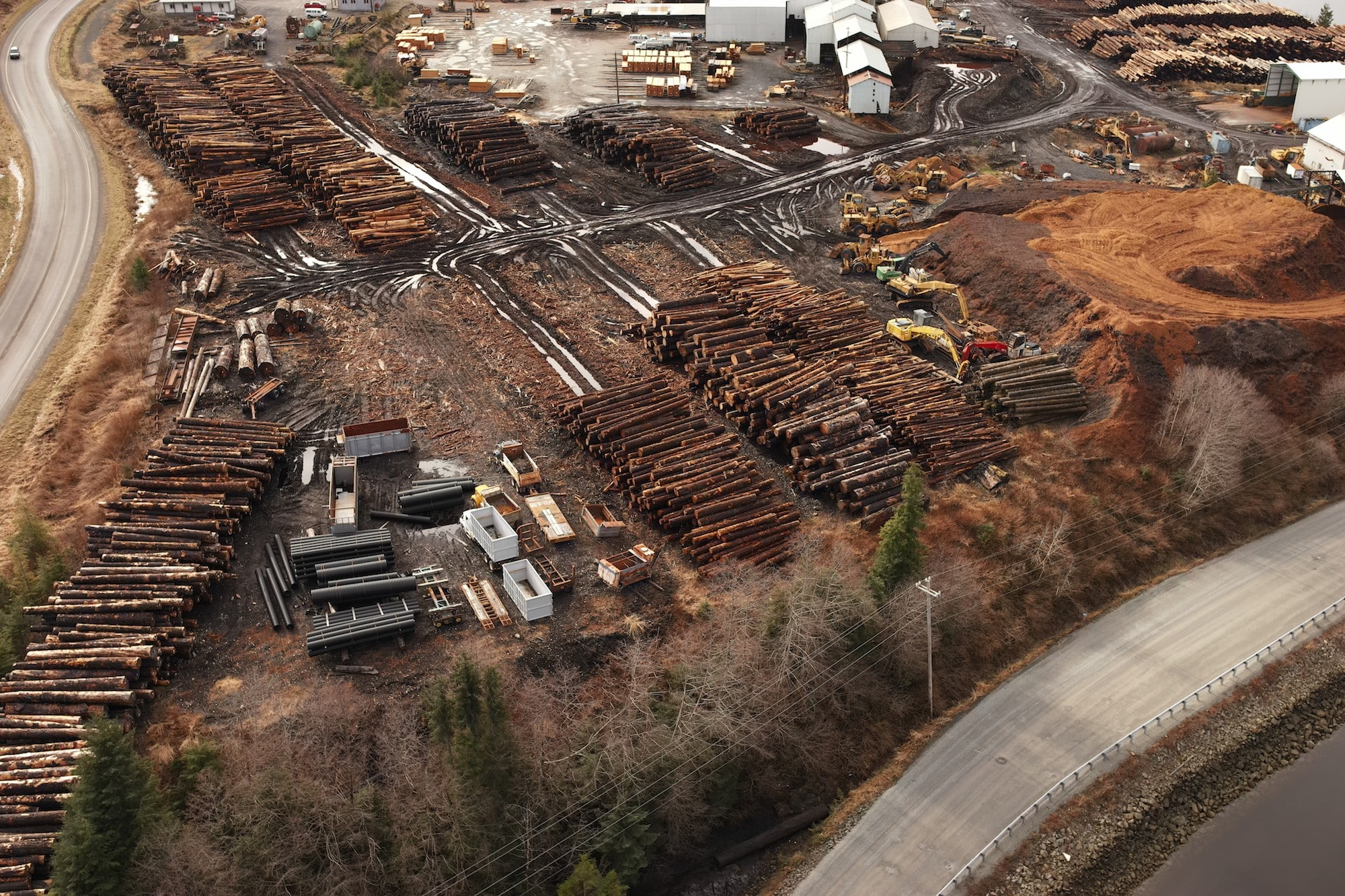 an aerial view of a lumberyard with many large piles of logs near a road