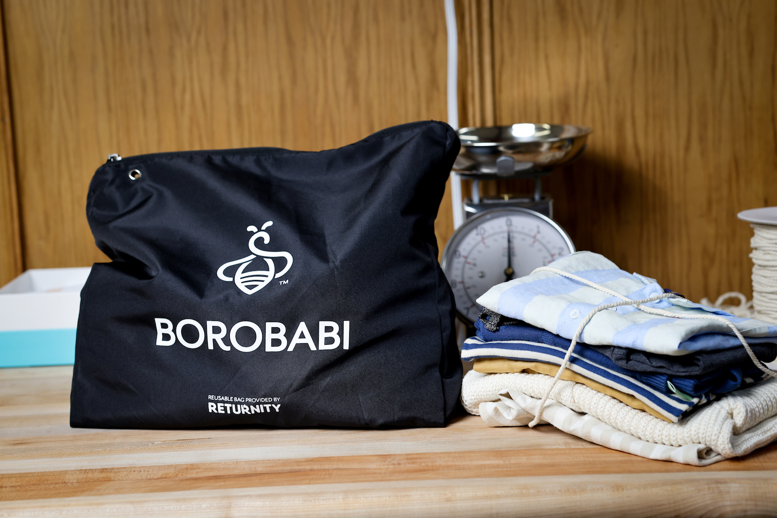 a black bag with the words "borobabi" in all caps on it next to a neatly folded pile of baby clothes tied up in string