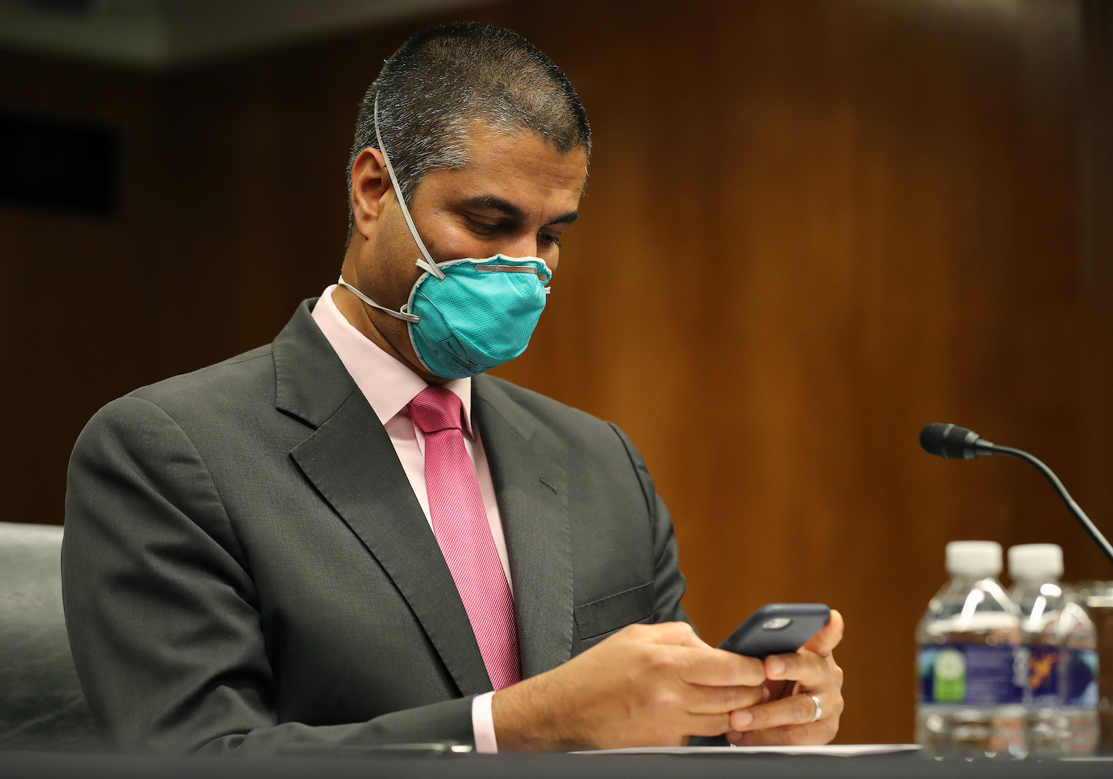 a man in a suit and green face mask looks at his cell phone