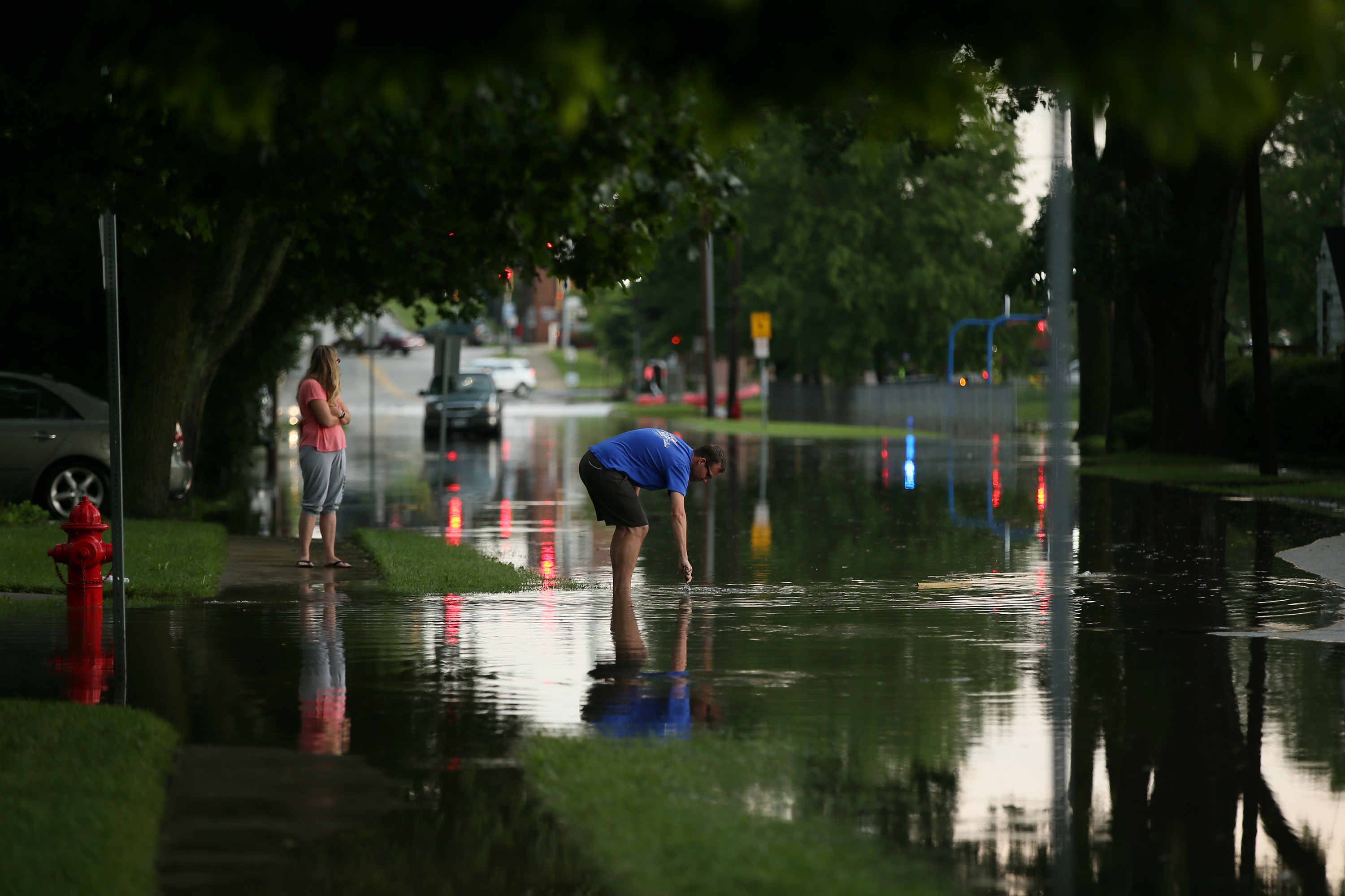 A man reaches down to unplug a sewer drain in a flooded street.