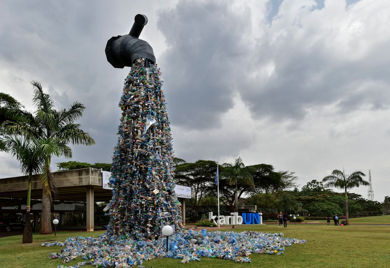 Sculpture made to look like a large water tap with a shower of plastic bottles coming out of it; palm trees in background