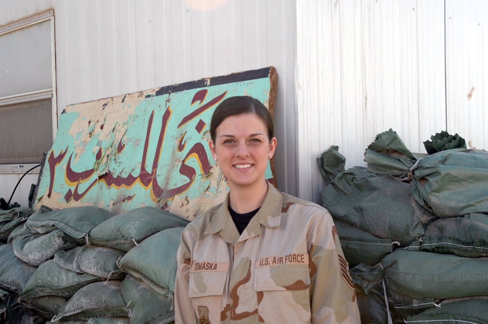 woman in a US Air Force uniform stands in front of sand bags and a sign in Arabic