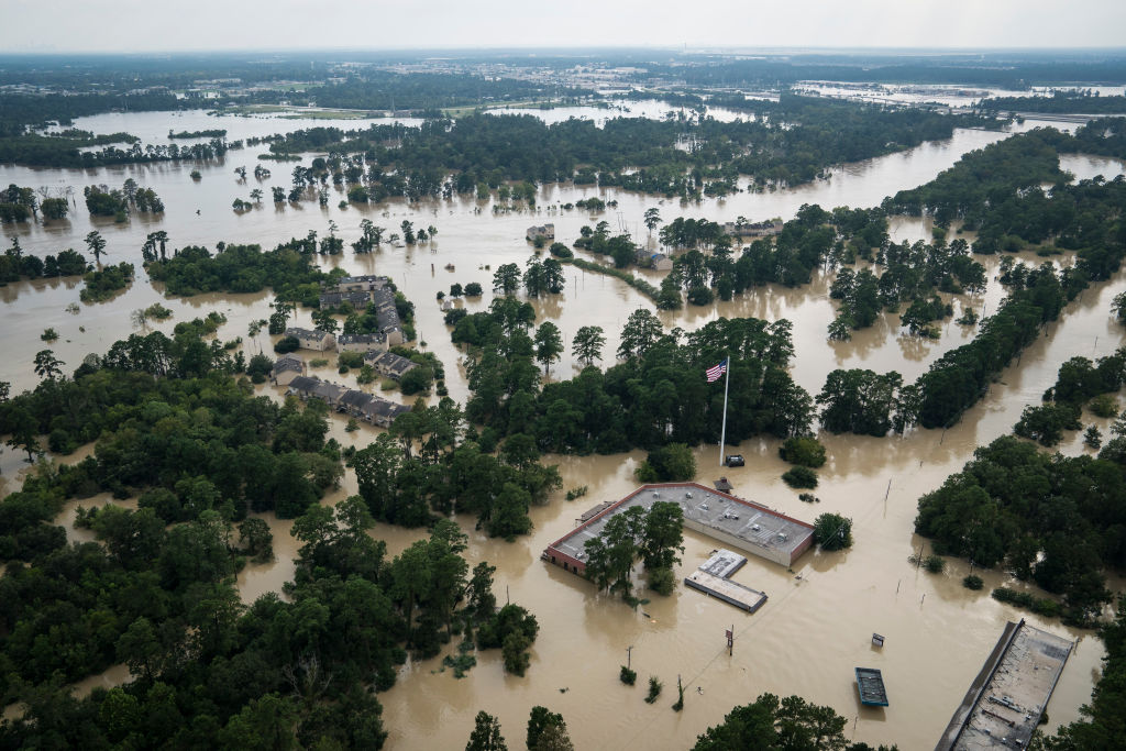 An aerial shot shows brown flood waters submerging trees and buildings.