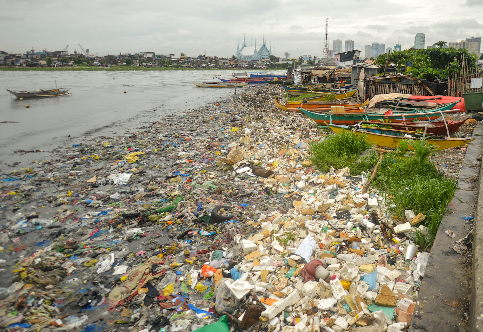 A riverbank littered with plastic and city in the background