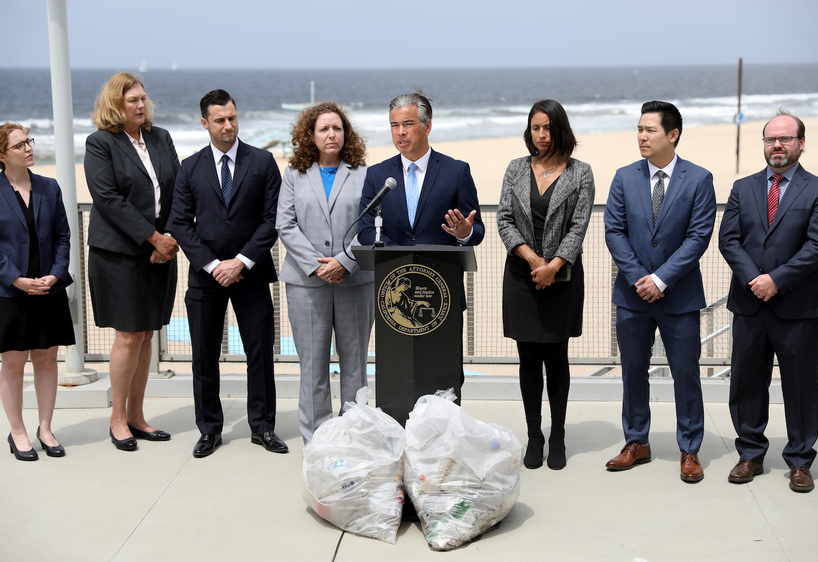 Attorney General Bonta speaks, surroundd by staff and with two garbage bags in front of him