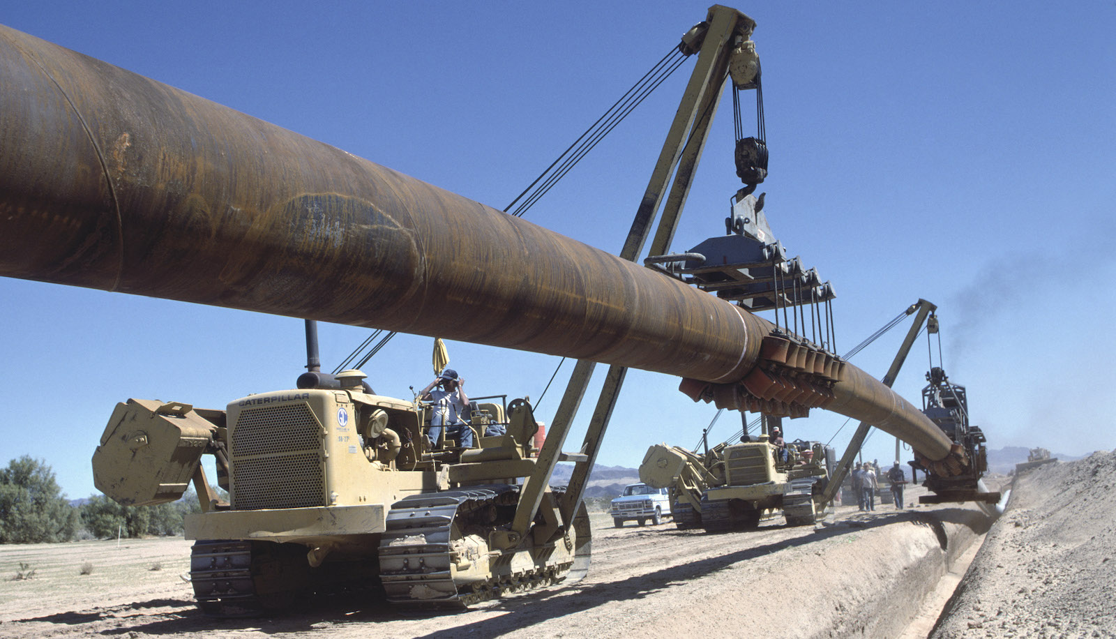A crane lifts a section of pipeline into a trench
