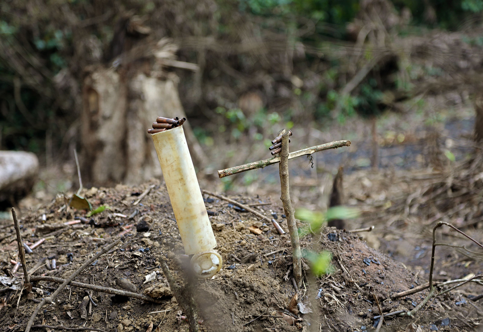 a mound of dirt with a plastic pipe and cross made of branches, both with bullet casings set on top of them