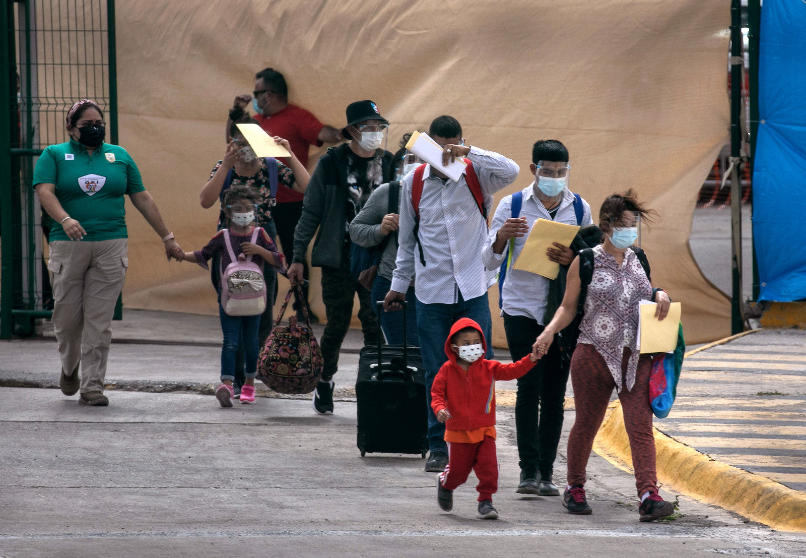 Mask-wearing asylum seekers carrying bags walk into the US
