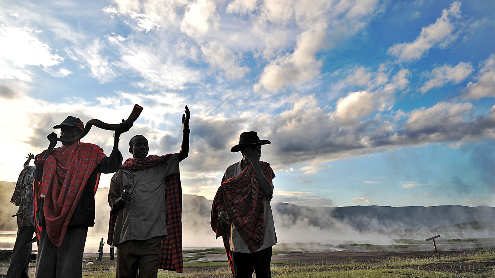 Four elders of the Endorois tribe, indigenous to Kenya, performing a ritual. Mist, mountains, and a blue sky with clouds are in the background