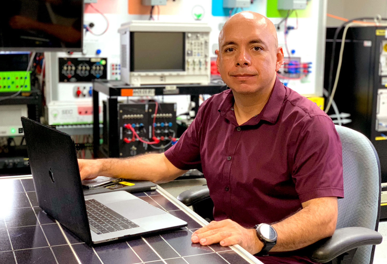Fabio Andrade, sentado en una mesa hecha de un panel solar, investiga microredes en Mayagüez, Puerto Rico.