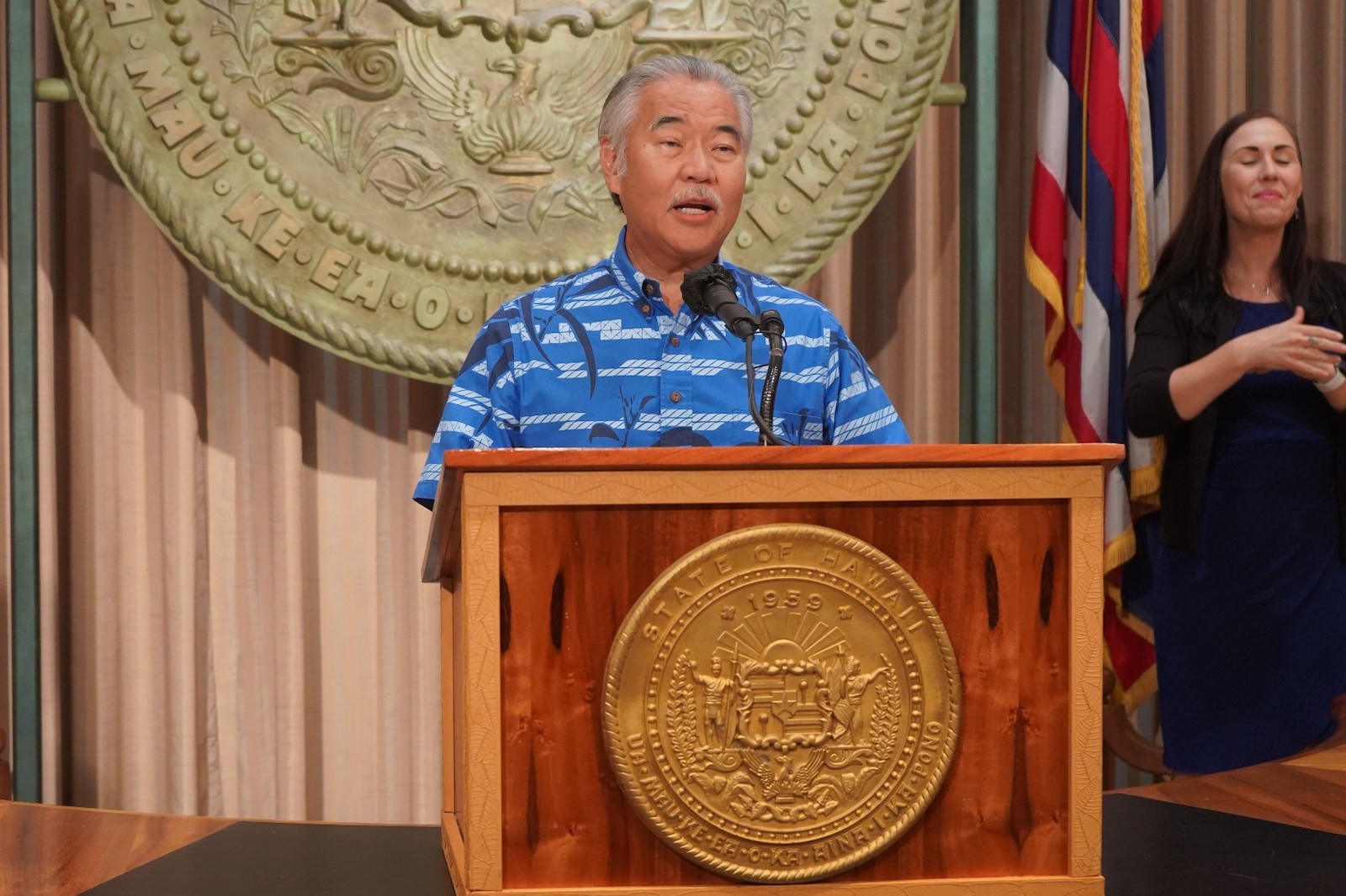 man speaks at podium with Hawaii seal