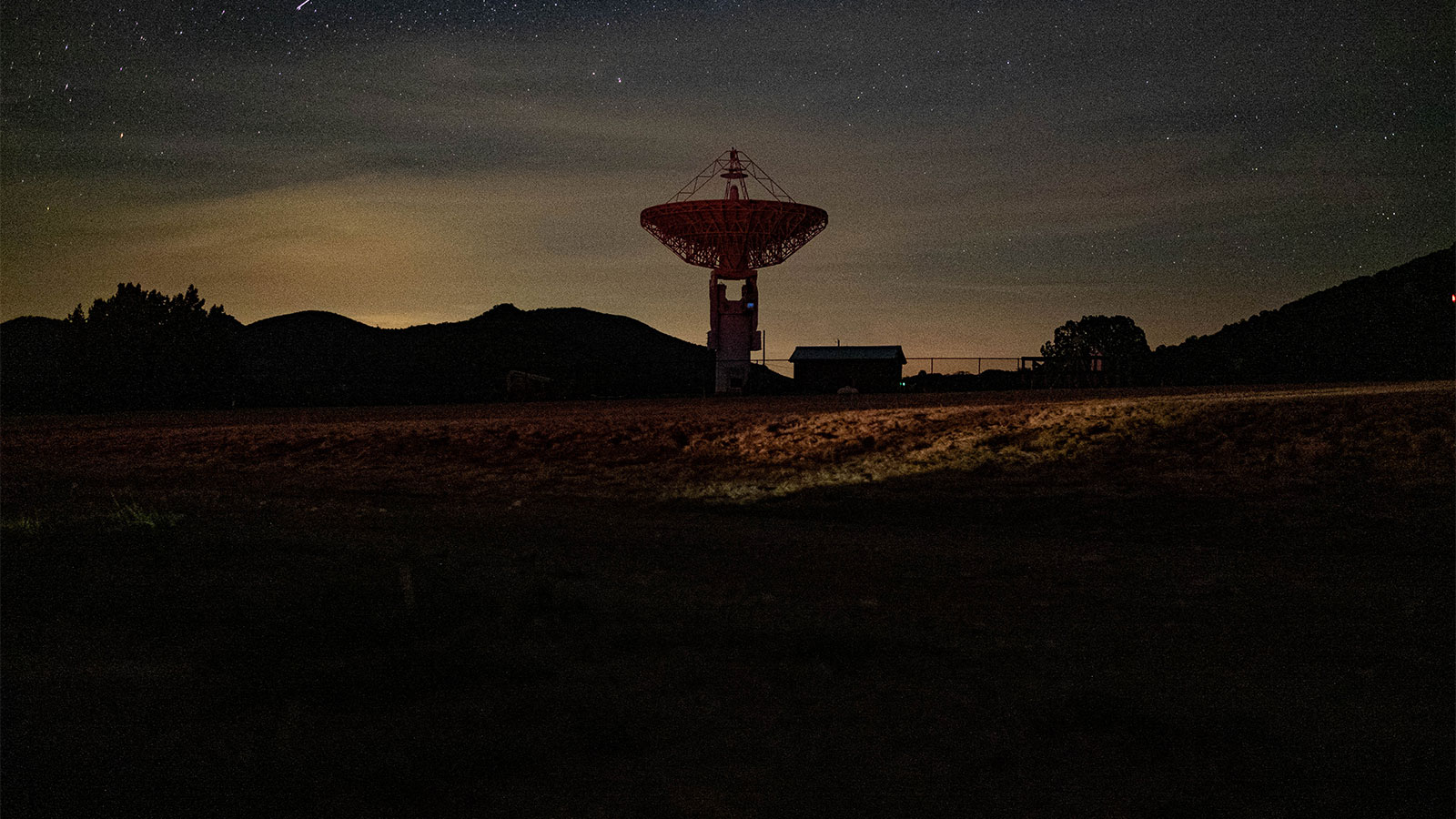 A picture of a large radio antenna with skyglow behind it, on the horizon.
