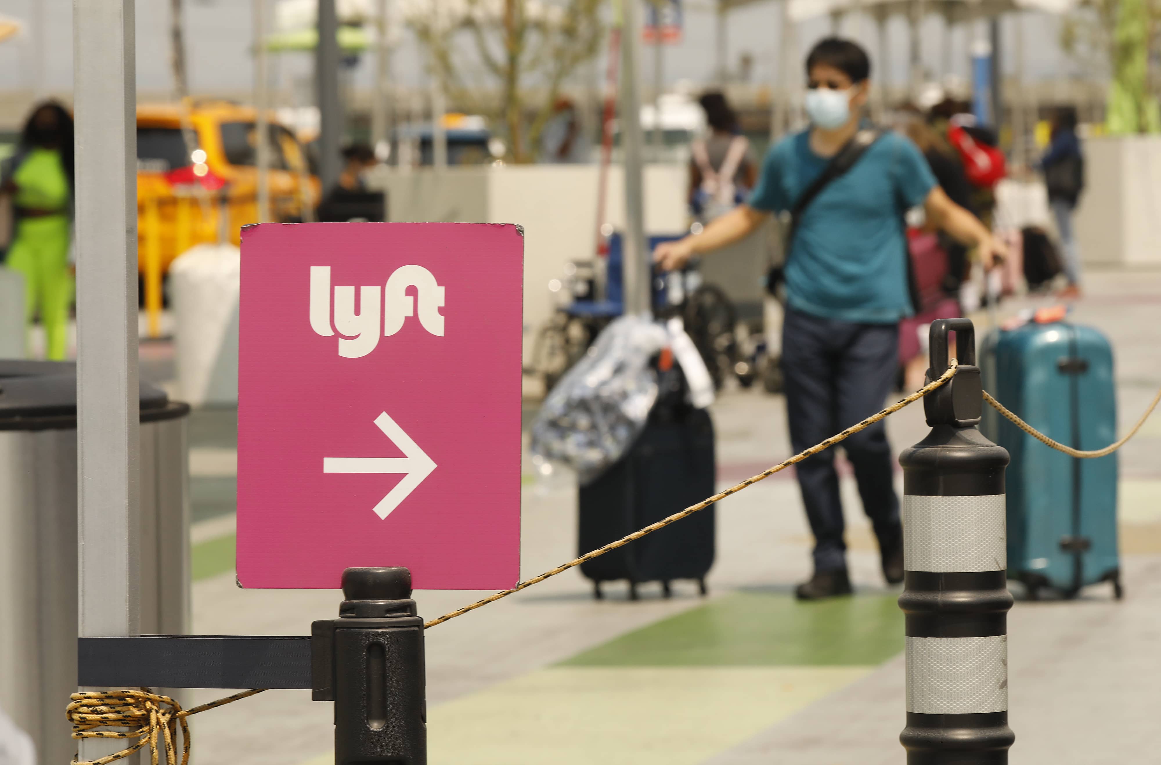 a lyft sign in the foreground and a woman walking with bags in the background
