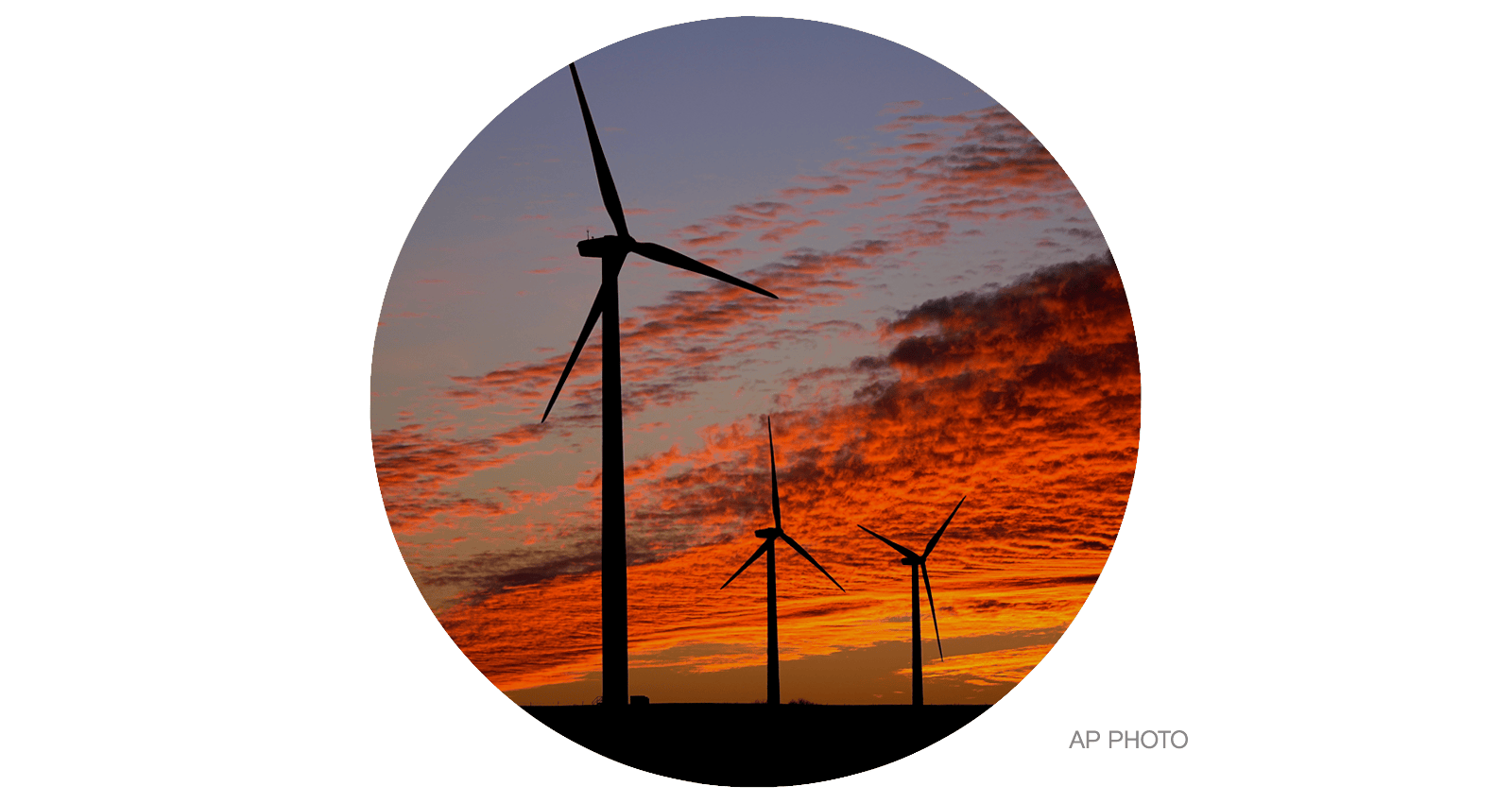 Wind turbines are silhouetted against the sky at sunset 